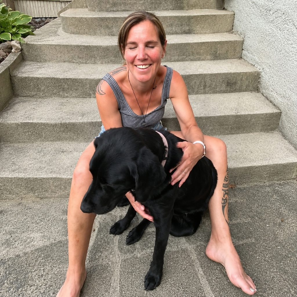 Hannah and her guide dog Dara sitting outside on steps. Hannah is wearing denim shorts and a black-and-white striped singlet.